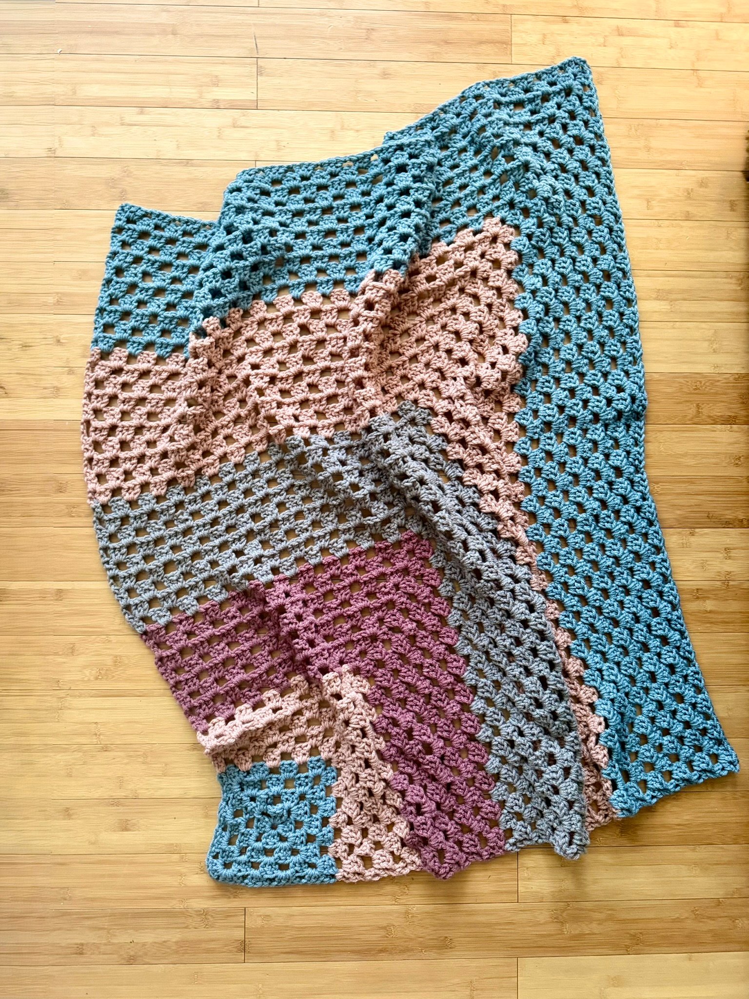 chunky granny stitch blanket in earthy tones on a wood floor