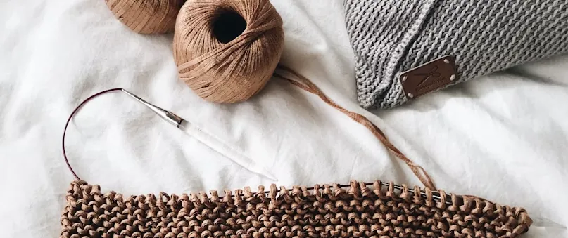 crochet hook on a bed with brown yarn and white blanket