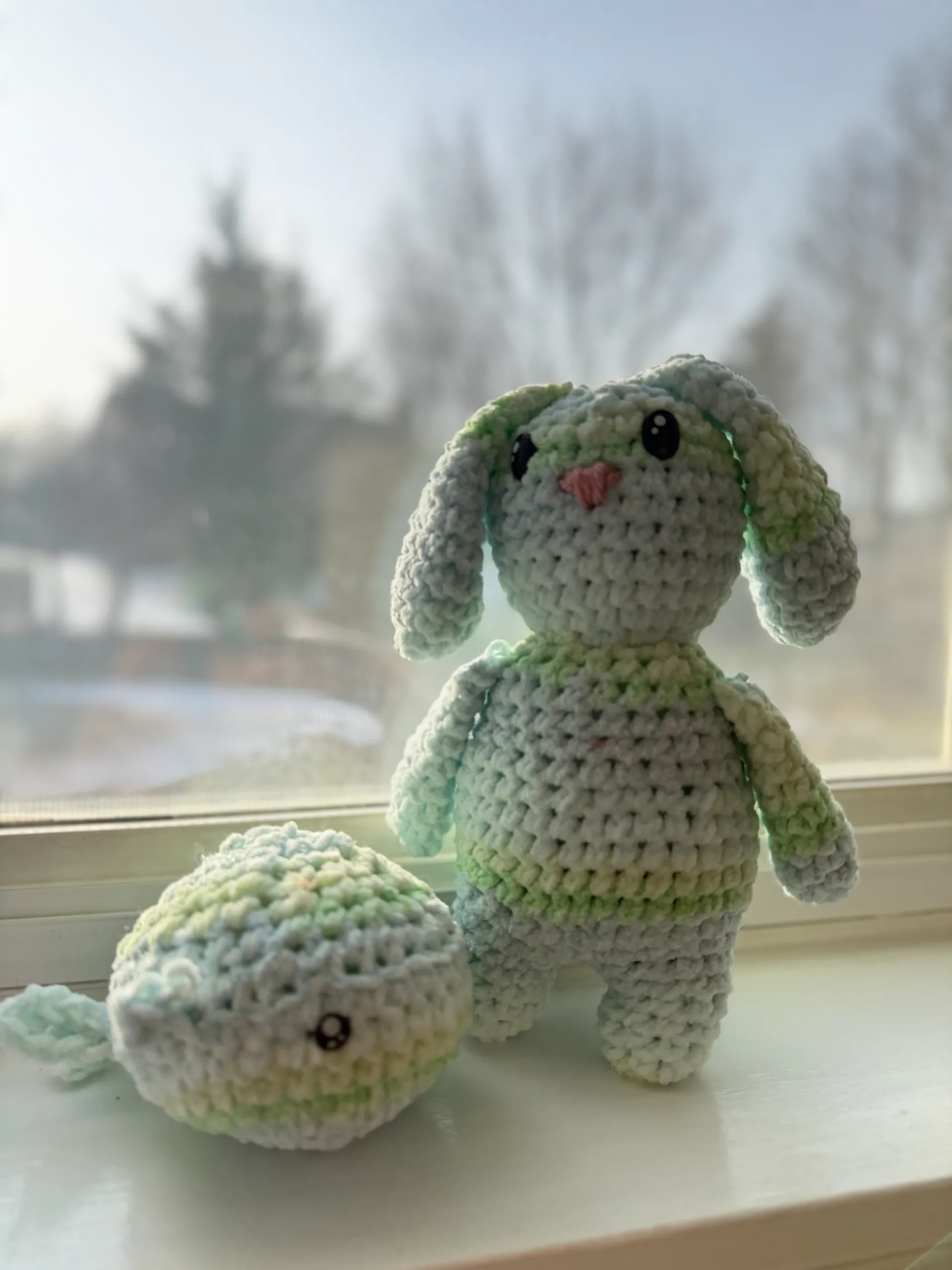 stash buster crochet plushie of a whale and a bunny by a window